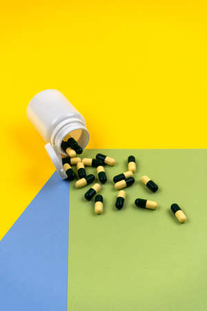 Medical pills scattered from a white jar on a colorful background. Color concept. Cosmetology and medicine concept. Herbal capsules. Vertical photo.の写真素材