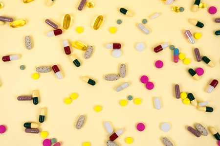 Background from multi-colored pills and capsules. Beige background strewn with medicines. Top view.の写真素材