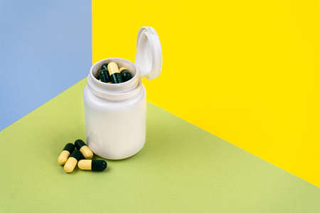 Yellow-green pills in a white jar on colored backgrounds. Food supplement, multivitamins, herbal medicines. Copy space.の写真素材