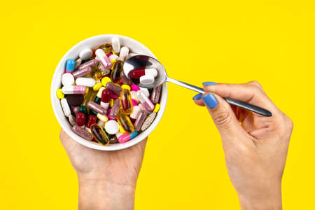 Heap of multi-colored pills in a plate. A young girl eats a spoon of medicines on a yellow background. Treatment concept. Top view.の写真素材