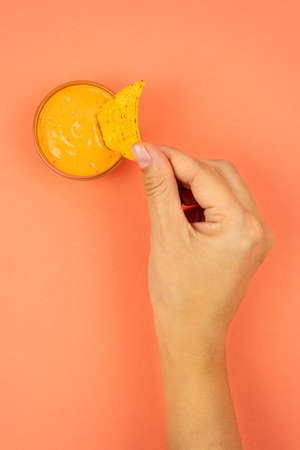 Delicious cheese sauce with nachos. A female hand lowers the nachos triangle with sauce.の写真素材