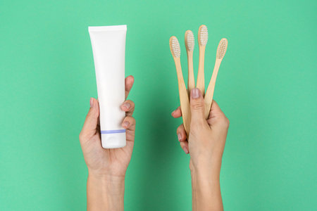 Bamboo toothbrushes and a tube of toothpaste in female hands on a mint background. Current trends in conscious consumption.の写真素材