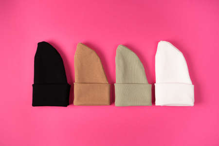 Beanie hats in the current basic colors of autumn and winter on a bright pink background are laid...