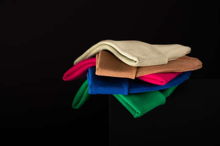 A collection of beanie hats in different bright colors stacked one on one on a dark contrasting...