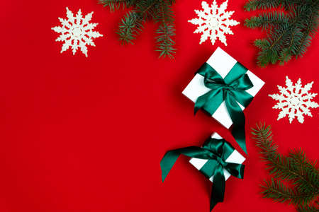 White gift boxes tied with a green satin ribbon with fir branches and snowflakes on a red...