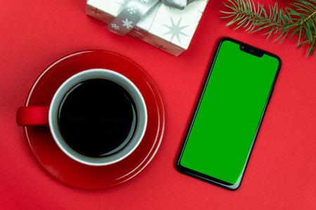 A mobile phone with a place for an inscription or drawing, with a red cup of coffee and gifts for the holiday and a pine branchの写真素材