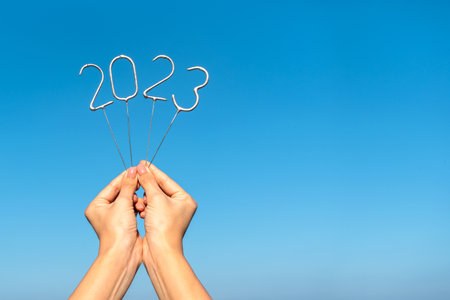 Figures for the upcoming New Year 2023 in women's hands against the background of a clear sky. Copy...