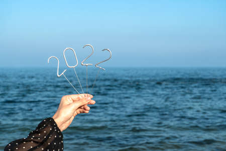 Figures of the upcoming New Year 2022 in a female hand against the background of the sea. Copy space.の写真素材
