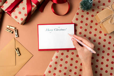 Top view on Christmas card with wishes in a red envelope on the background of gift wrapping. Girl writing letterの写真素材