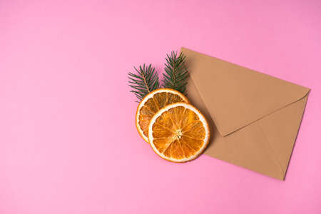 Holiday and invitation layout. Blank card in a craft envelope on a pink background with spruce sprigs and orange slices. Copy spaceの写真素材