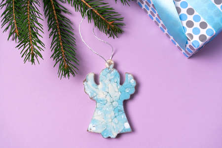 A blue angel hangs on a spruce branch. Epoxy resin christmas tree decorations with gift on purple background.の写真素材