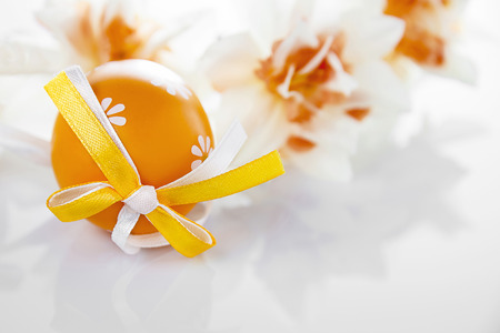 Orange Easter egg and daffodils on a white backgroundの写真素材