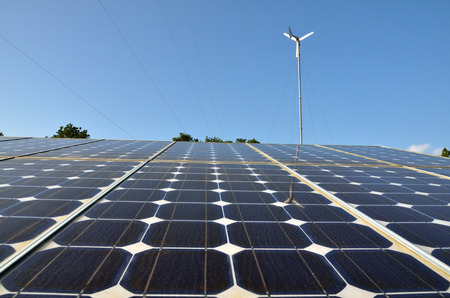 Solar panels and wind turbine against blue skyの写真素材