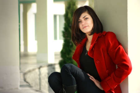 a sitting beautiful young girl is in a red overcoat