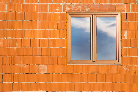 Wall texture made of several layers of orange bricks with negative space and window on the left with reflection of sky の写真素材
