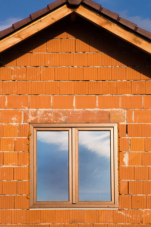 Wall texture made of several layers of orange bricks with roof and window on the left with reflection of sky の写真素材