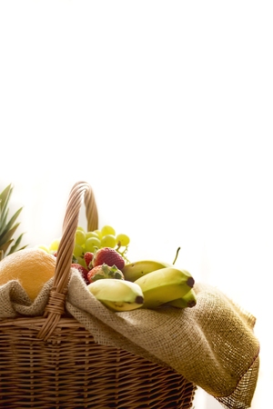 Horizontal closeup detail of a basket full of fruit (banana, strawberry, pineapple, orange, pear, apple) isolated on white background - high keyの写真素材