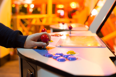 Detail of player hand interacting and playing with joysticks and buttons on an old arcade game in a gaming roomの写真素材