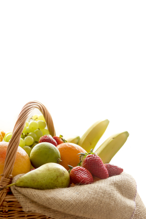 Vertical closeup detail of a basket full of fruit (banana, strawberry, pineapple, orange, pear, apple) isolated on white background - high keyの写真素材