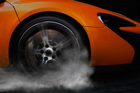 Orange super sport car from side with detail on spinning wheel, smoking and doing burnouts on a dark backgroundの写真素材