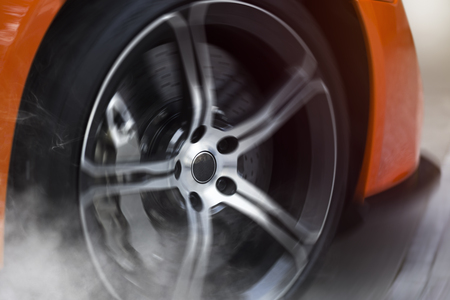 Orange Sport Car with detail on spinning and smoking wheels/tires doing burnouts, dynamic photoの写真素材