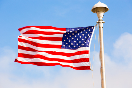 Flag of United States of America wawing in the wind with a blue background and cloudy sky