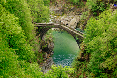 Top view on the Ponte Romano Intragna Bridge hiding in the valley with beautiful river covered with trees, close to Verzasca village. It is the oldest bridge in Switzerland.の写真素材