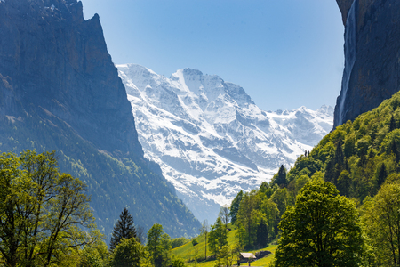 Scenic view on mountains behind historic village Lauterbrunnen. Gigantic mountains covered with snow with waterfall and green grass in Bern canton, Switzerlandの写真素材