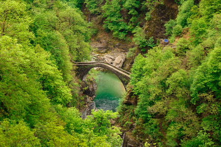 Top view on the Ponte Romano Intragna Bridge hiding in the valley with beautiful river covered with trees, close to Verzasca village. It is the oldest bridge in Switzerland.の写真素材