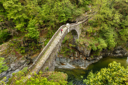 Top view on the Ponte Romano Intragna Bridge hiding in the valley with beautiful river covered with trees, close to Verzasca village. It is the oldest bridge in Switzerland.の写真素材