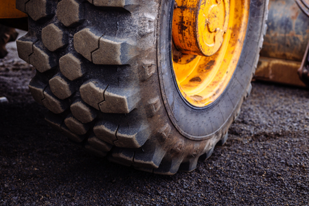 Detail on tire track pattern on a yellow heavy duty digger excavator on a dark soil