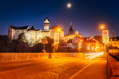 Czech Castle Loket in winter, long night exposure with beautiful blue sky and yellow street christmas city lights glowing on a bridge towards the city.のeditorial素材