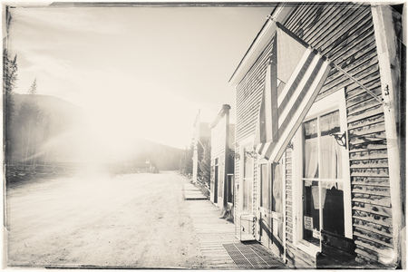 Black and White Sepia Vintage Photo of Old Western Wooden Buildings with flag of the united states, in St. Elmo Gold Mine Ghost Town in Colorado, USA hidden in mountainsの写真素材