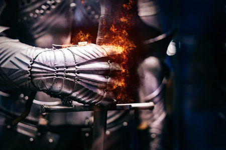 Close up of a Medieval steel armour with iron glove hand bursting with flames of fire, holding a giant swordの写真素材