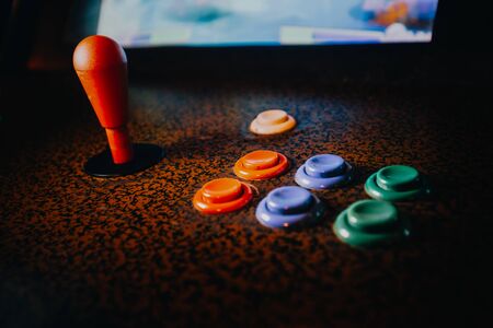 Detail on a joystick and button controls of a vintage arcade video game in a dark room with dark...