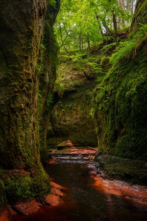 Inside of the Devilâs Pulpit gorge, with beautiful running water and red river bed with walk in the water towards a waterfall, near Glasgow, Scotland, UKの写真素材