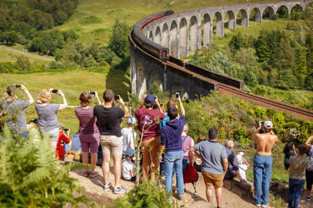 Glenfinnan Viaduct, Scotland, UK - 26 July, 2019: Crowds of tourists photographing Glenfinnan Viaduct surrounded by mountains during sunny dayのeditorial素材