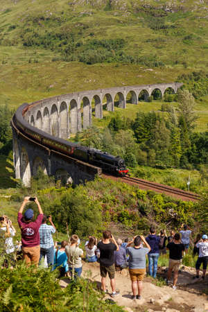 Glenfinnan Viaduct, Scotland, UK - 26 July, 2019: Crowds of tourists photographing Glenfinnan Viaduct surrounded by mountains during sunny dayのeditorial素材