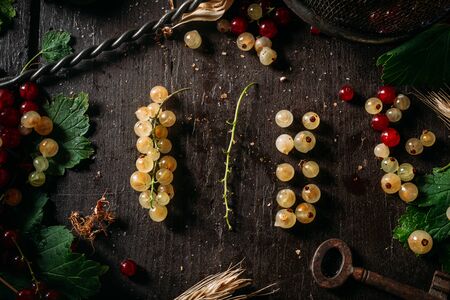 Bunch of white currant disassembled with mix of red and white currant around, laying on a dark wooden tableの写真素材