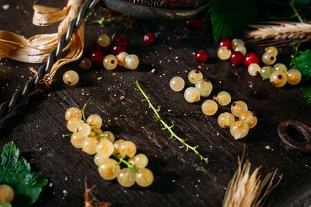 Bunch of white currant disassembled with mix of red and white currant around, laying on a dark wooden tableの写真素材
