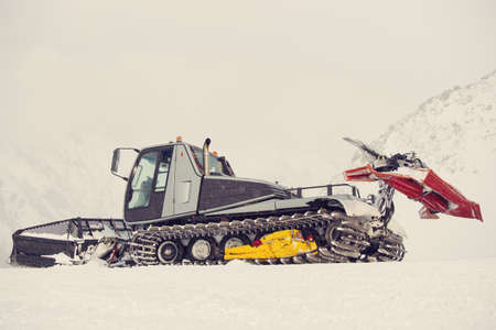 Snow plow on a ski resort with a young man in its caterpillar chain