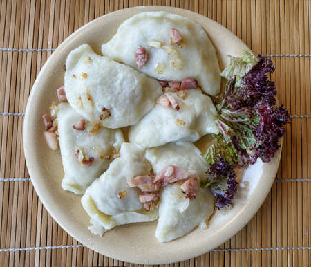 Traditional polish Pierogi stuffed dumplings served on a terracota plate and decorated with ham and...
