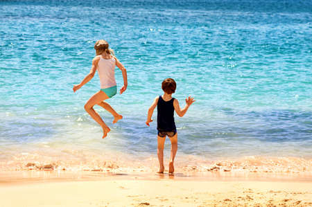 Two kids playing jumping in the sea waves on a sand beach on a warm sunny summer dayの写真素材