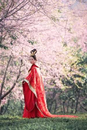 Beautiful Chinese young woman wearing red traditional cheongsam in cherry blossoms gardenの写真素材