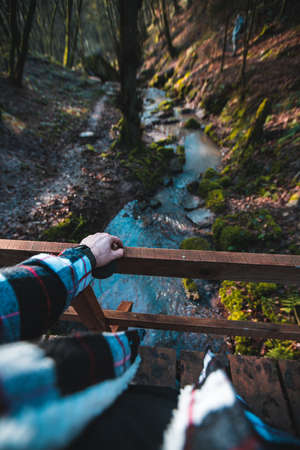 Man standig on a wooden Bridge looking down a small streamの写真素材