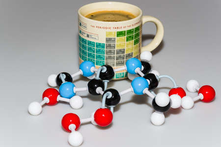 Caffeine and water molecules in front of a Periodic table coffee mug on white-gray backgroundの写真素材