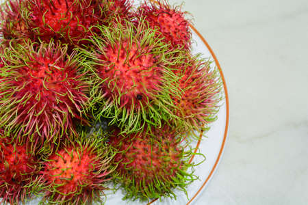 Red rambutan on white dish. Fruit tropical tree of the family Sapindaceae , native to South - East Asia , cultivated in many countries in the region, on marble backgroundの写真素材