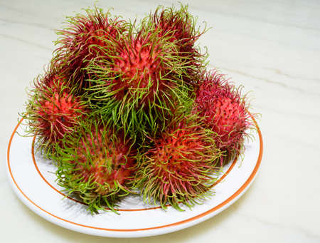 Red rambutan on white dish. Fruit tropical tree of the family Sapindaceae , native to South - East Asia , cultivated in many countries in the region, on marble backgroundの写真素材