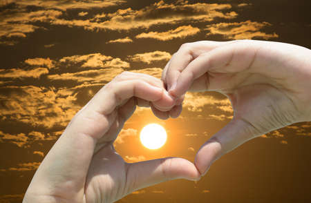 Girl hand in heart form love on sunset skyの写真素材