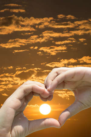 Girl hand in heart form love on sunset skyの写真素材